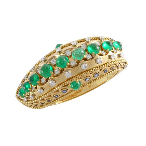 Gold, cabochon emerald, sapphire and diamond Indianesque bangle by Cartier, Paris, the upper section in the form of a bold gold leaf cap studded with a line of nine graduated sugarloaf and round cabochon emeralds,